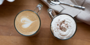Two specialty coffee drinks at Mad Hatter Cafe & Bakeshop in Durham: one with artistic latte art and the other topped with whipped cream and chocolate sprinkles