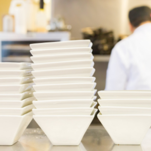 Stack of clean white plates ready for service in the bustling kitchen of Mad Hatter Cafe & Bakeshop, Durham