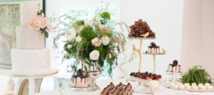 Elegant wedding catering setup featuring a variety of cakes and desserts, beautifully arranged with floral decorations at Mad Hatter Cafe & Bakeshop in Durham